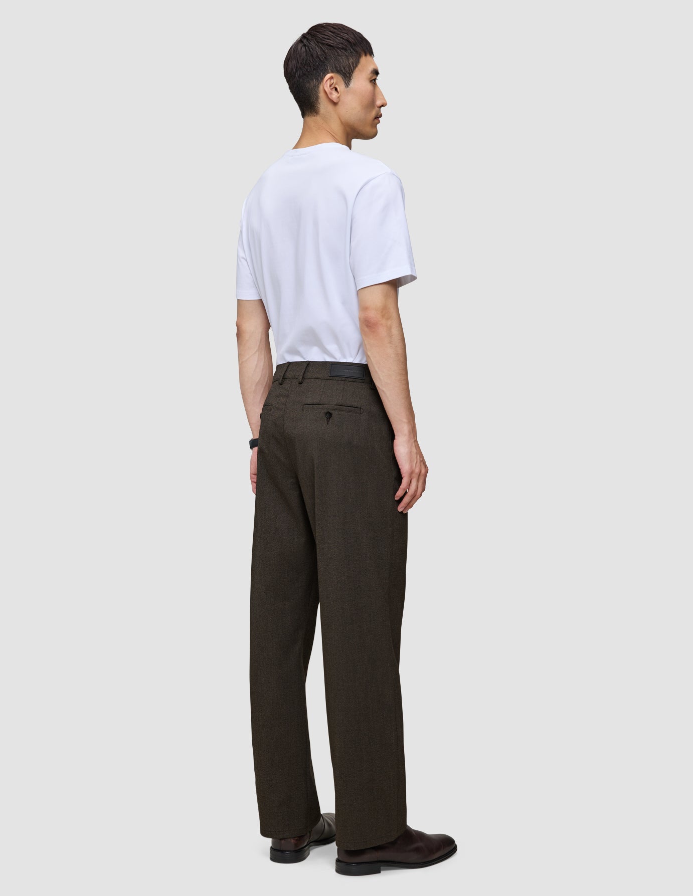 A man viewed from the side, wearing a white t-shirt and Atelier Pants Relaxed Dark Brown in heavyweight broken twill.