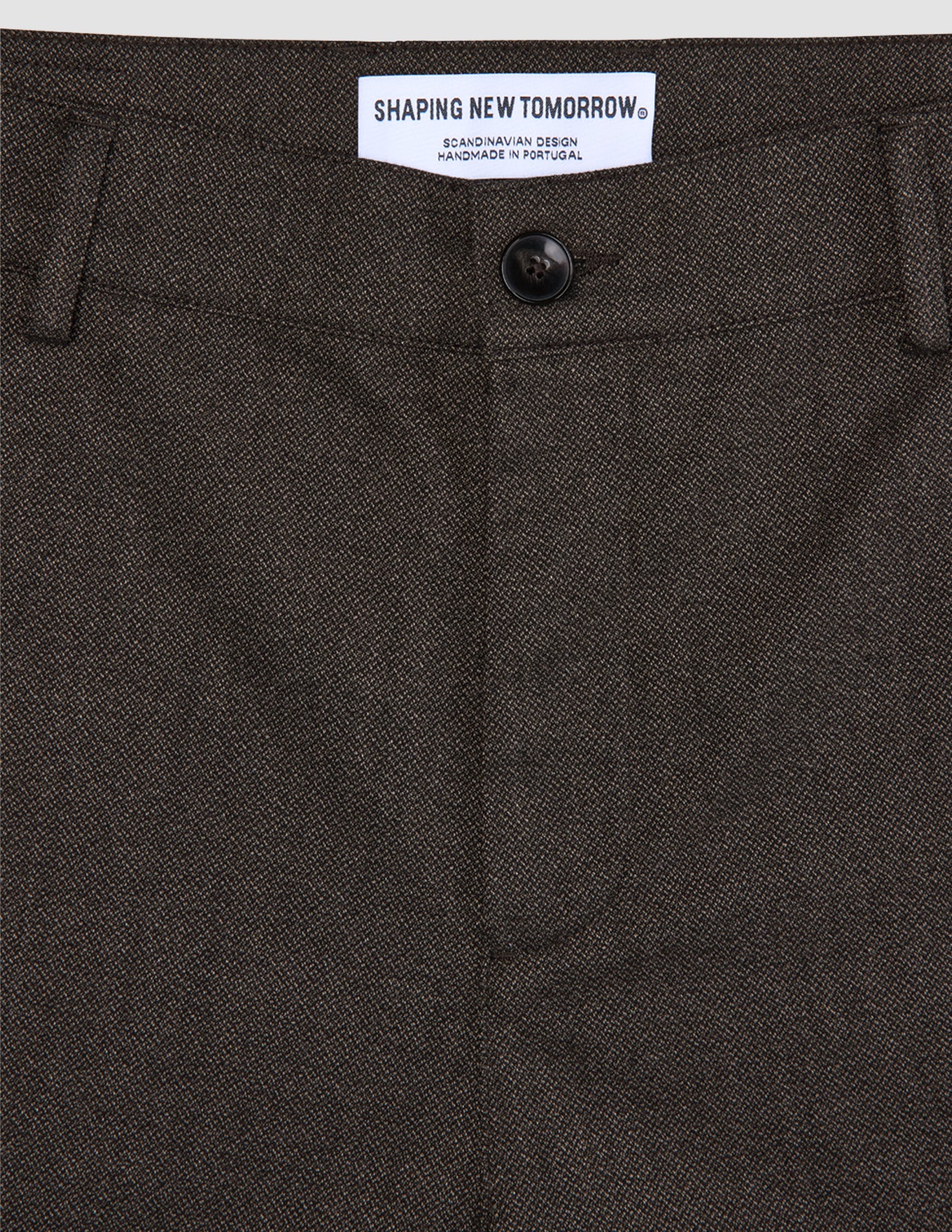 Close-up of dark brown Atelier Pants Relaxed Dark Brown in heavyweight broken twill, featuring a button closure and a brand label at the waistband.