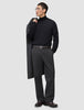 A man wearing a black turtleneck and Atelier Pants Relaxed Dark Grey in heavyweight broken twill, holding a coat over his shoulder.