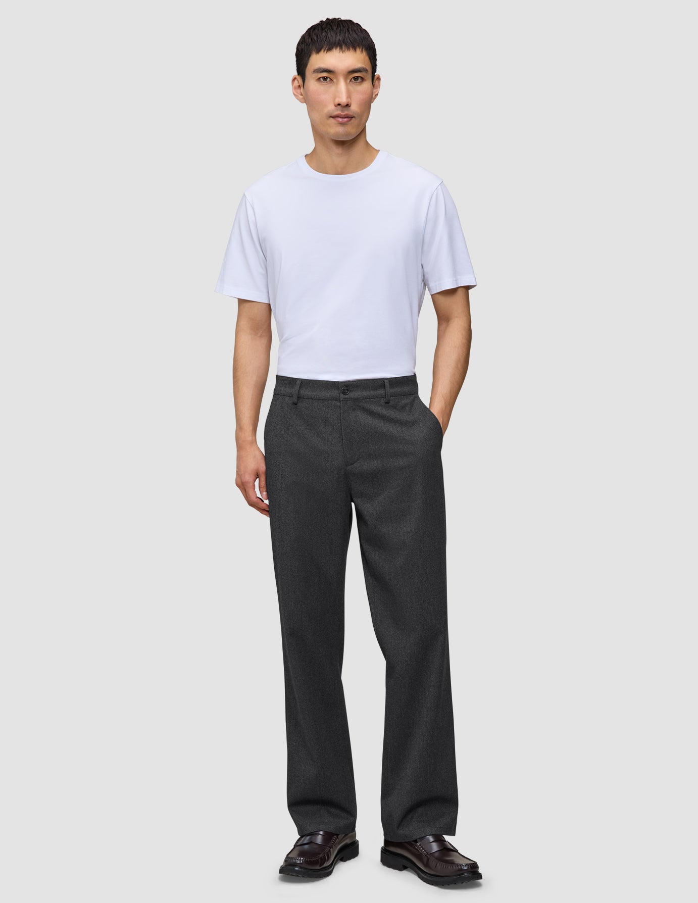A man in a white t-shirt and Atelier Pants Relaxed Dark Grey made from heavyweight broken twill, finished with dark leather loafers.