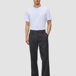 A man in a white t-shirt and Atelier Pants Relaxed Dark Grey made from heavyweight broken twill, finished with dark leather loafers.