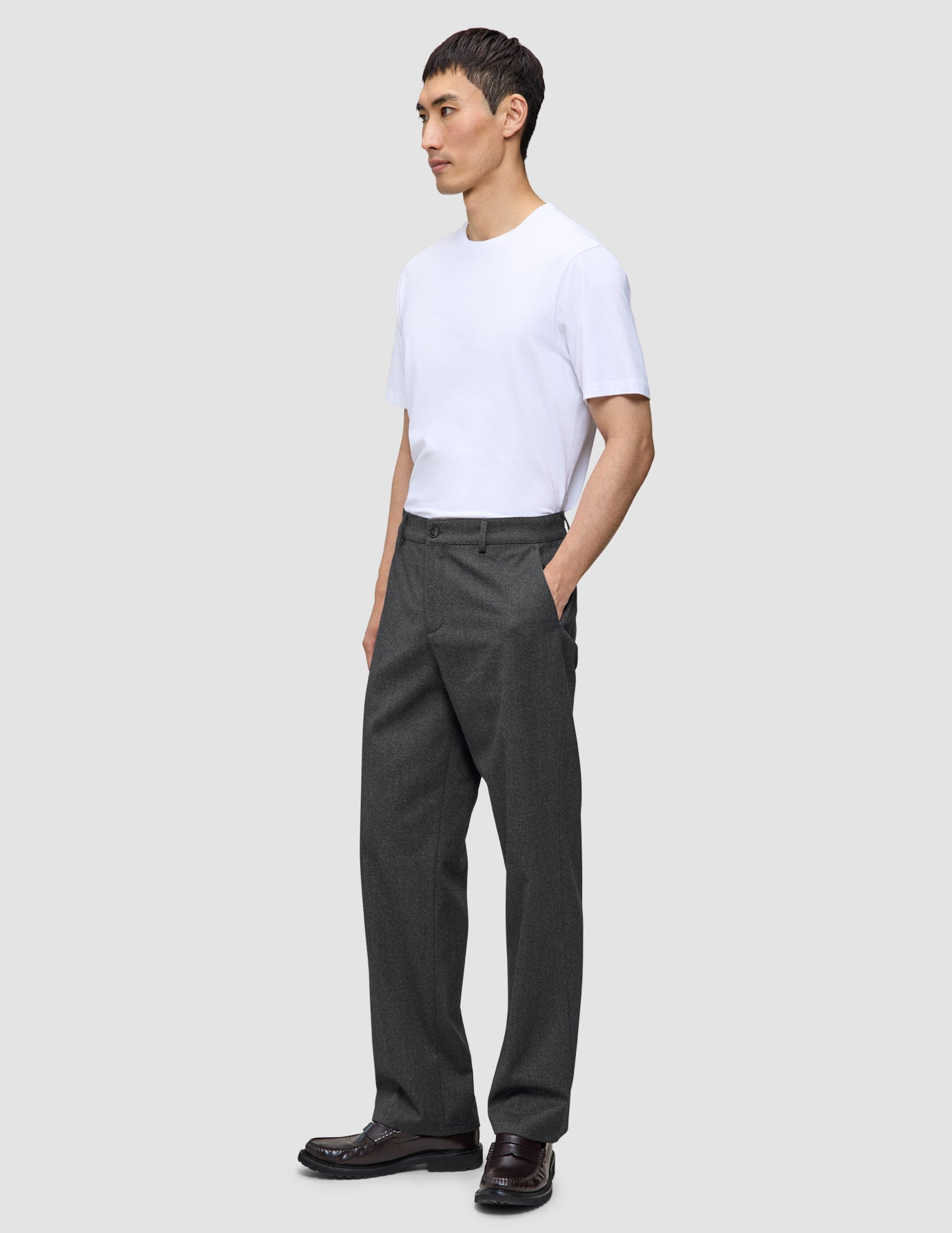 A man wearing a white t-shirt and dark grey Atelier Pants Relaxed in heavyweight broken twill, with his hand in his pocket.