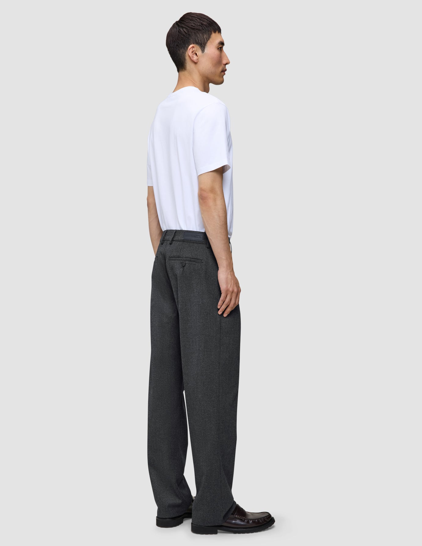 Profile view of a person wearing a white t-shirt, leather loafers, and dark grey Atelier Pants Relaxed in a relaxed fit, heavyweight broken twill.