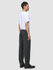 Profile view of a person wearing a white t-shirt, leather loafers, and dark grey Atelier Pants Relaxed in a relaxed fit, heavyweight broken twill.