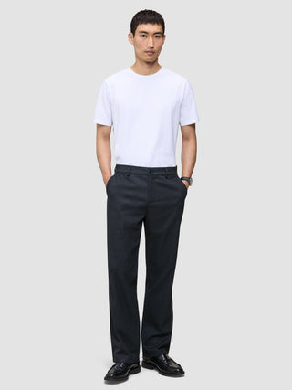 A person wearing a white t-shirt and Atelier Pants Relaxed Dark Navy with their hands in their pockets.