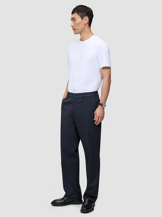 A man wearing a white t-shirt and Atelier Pants Relaxed Dark Navy, which are relaxed-fit, heavyweight broken twill trousers.