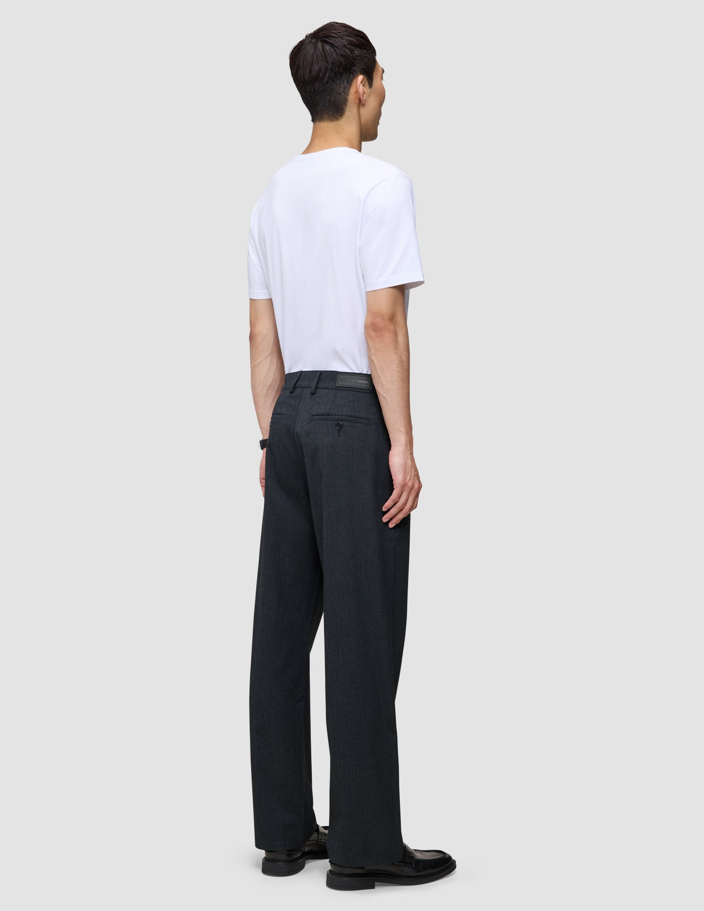 A man seen from behind wearing a white t-shirt and Atelier Pants Relaxed Dark Navy in heavyweight broken twill, paired with black shoes.