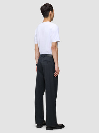 A man seen from behind wearing a white t-shirt and Atelier Pants Relaxed Dark Navy in heavyweight broken twill, paired with black shoes.