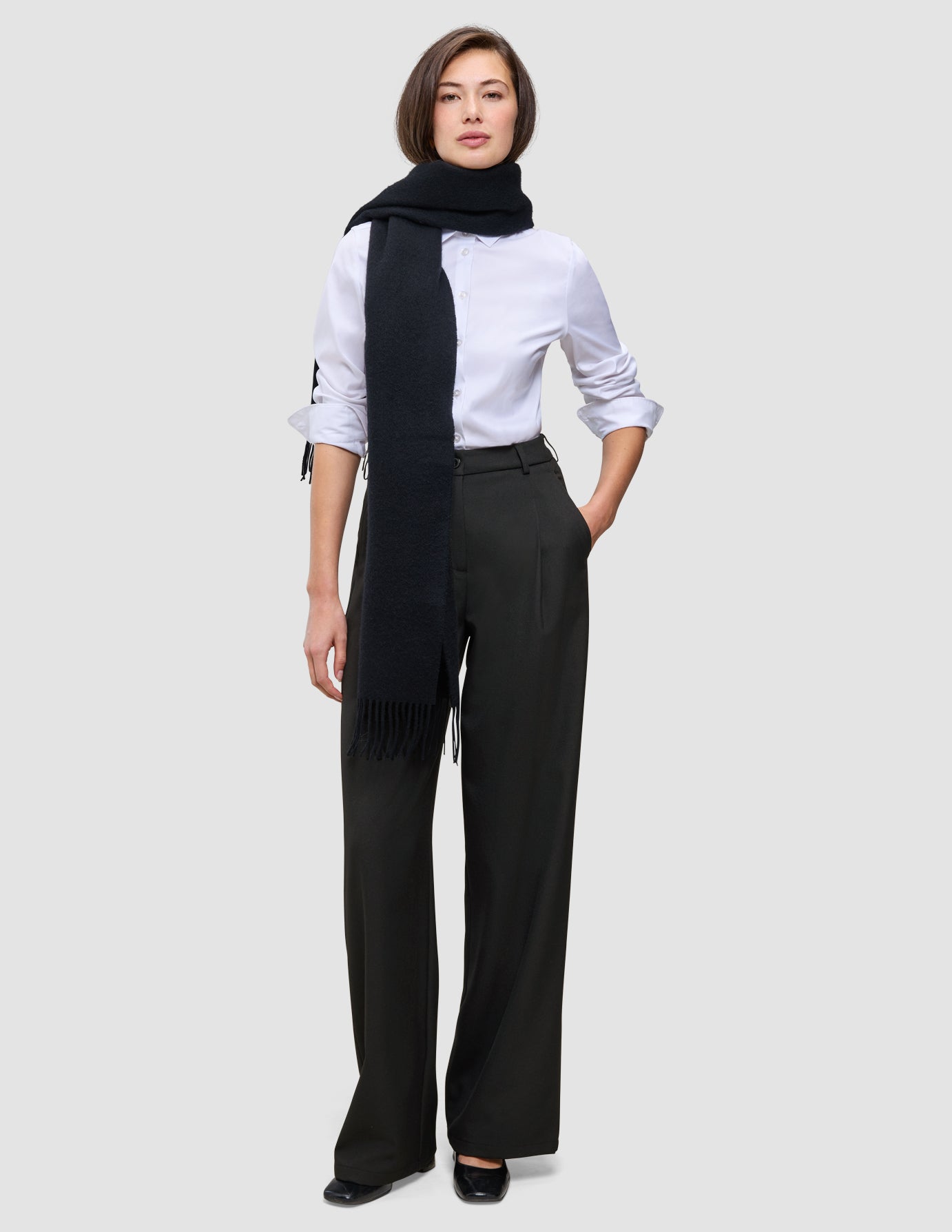 A woman wearing a white button-down shirt, a long black scarf, and Women’s Avira Pants Wide Black with her hand in her pocket.