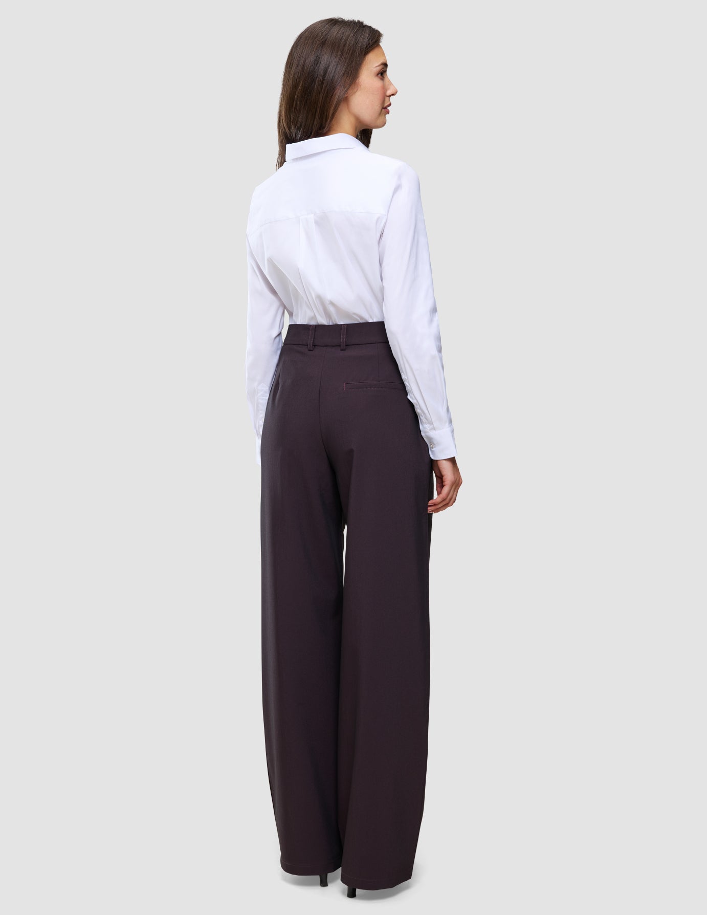 A person viewed from the back wearing a white button-down shirt tucked into Women’s Avira Pants Wide Burgundy Berry.