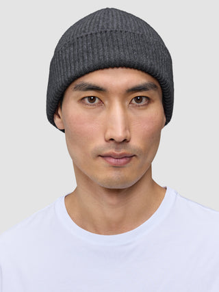 A person wearing a dark grey merino wool rib knit Beanie Dark Grey.