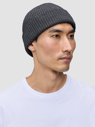 A person wearing a dark grey merino wool rib knit Beanie Dark Grey.