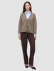 A woman wearing a Women’s Chunky Soft Wool Knit Cardigan Taupe Melange over a light blue button-down shirt, paired with dark brown trousers and matching heels.