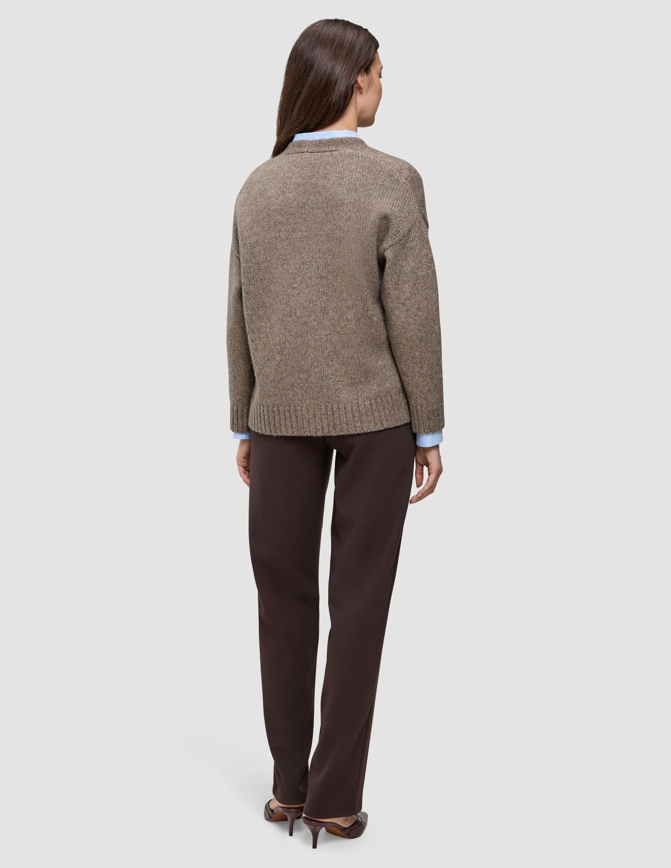 A person wearing a Women’s Chunky Soft Wool Knit Cardigan Taupe Melange over a light blue collared shirt and dark brown trousers.