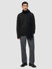 A man wearing a Chunky Soft Wool Knit Crewneck Black, a dark scarf, grey trousers, and black shoes.