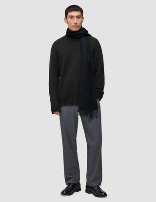 A man wearing a Chunky Soft Wool Knit Crewneck Black, a dark scarf, grey trousers, and black shoes.