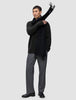 A man wearing a Chunky Soft Wool Knit Crewneck Black sweater in dark olive, grey trousers, and a black scarf draped over one shoulder.