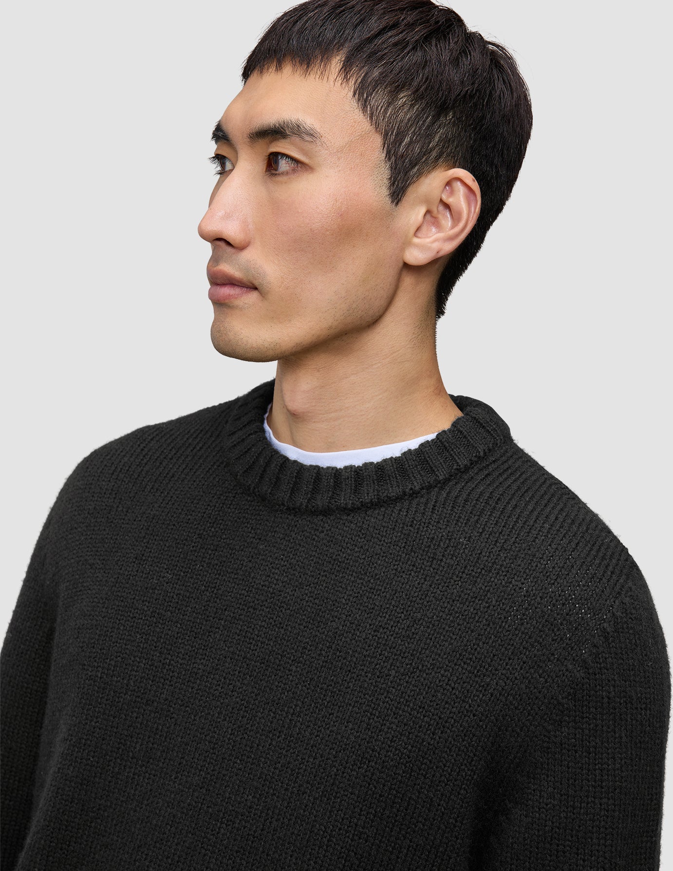 A man wearing a black Chunky Soft Wool Knit Crewneck over a white shirt, reflecting a clean Scandinavian design.