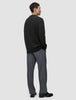 A man standing sideways wearing a Chunky Soft Wool Knit Crewneck Black sweater and grey trousers.