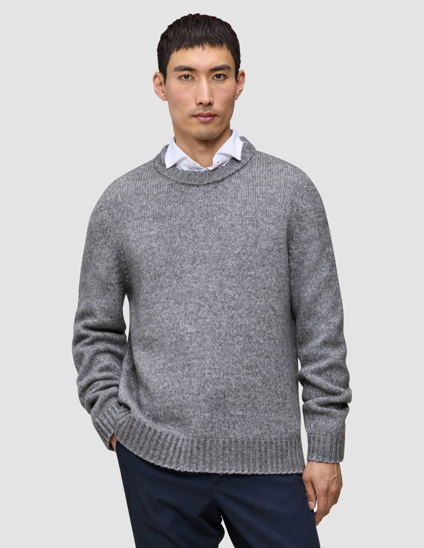 A man wearing a Chunky Soft Wool Knit Crewneck Glacier Grey sweater over a white collared shirt.
