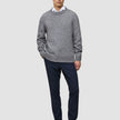 A man wearing a Chunky Soft Wool Knit Crewneck Glacier Grey sweater over a white collared shirt, dark trousers, and dark loafers.