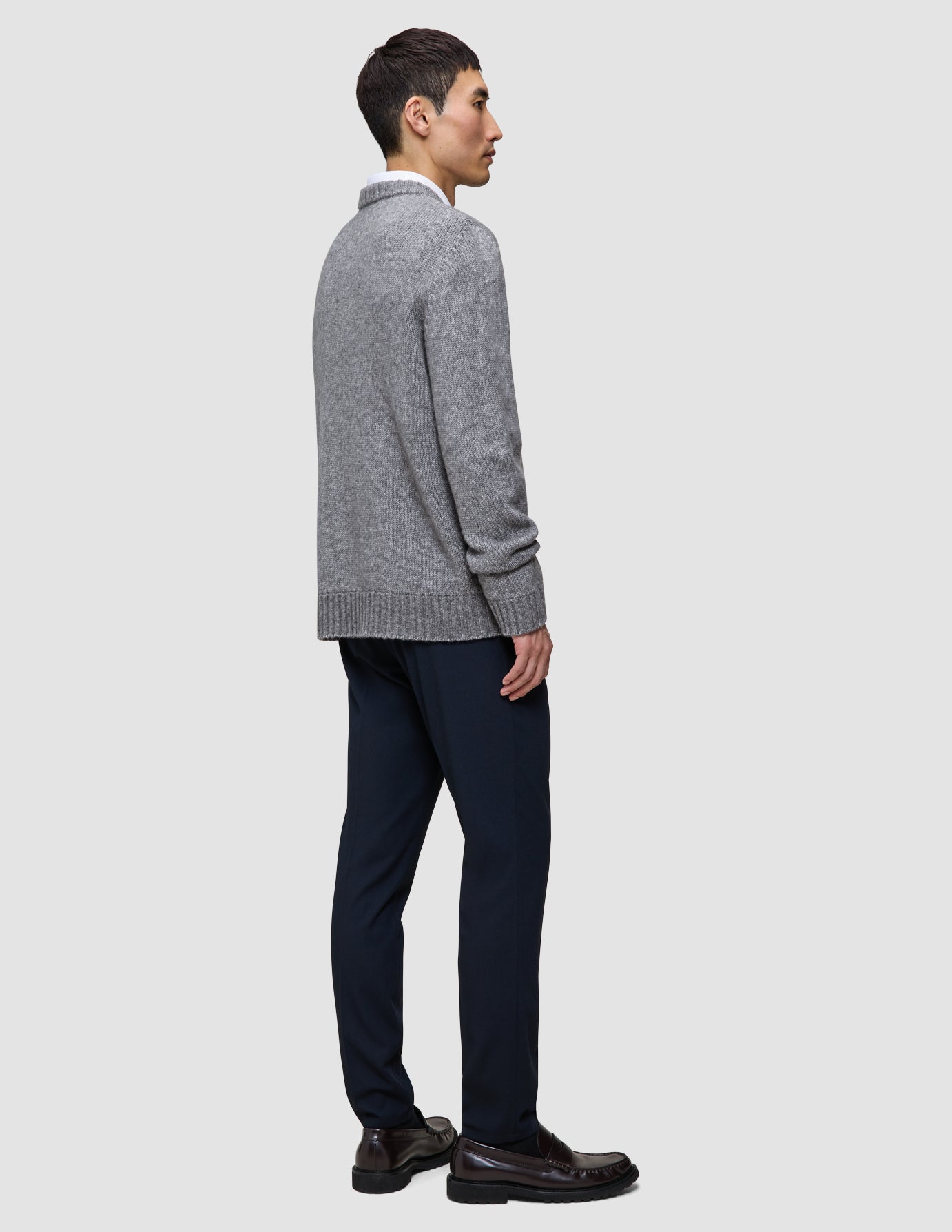A person in profile wearing a Chunky Soft Wool Knit Crewneck Glacier Grey over a collared shirt, dark trousers, and brown loafers.