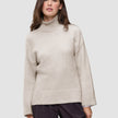 A woman wearing the Women’s Chunky Soft Wool Knit Turtleneck Sugar Melange, an oversized, light beige merino wool sweater with ribbed cuffs and hem in a minimalist Scandinavian design.