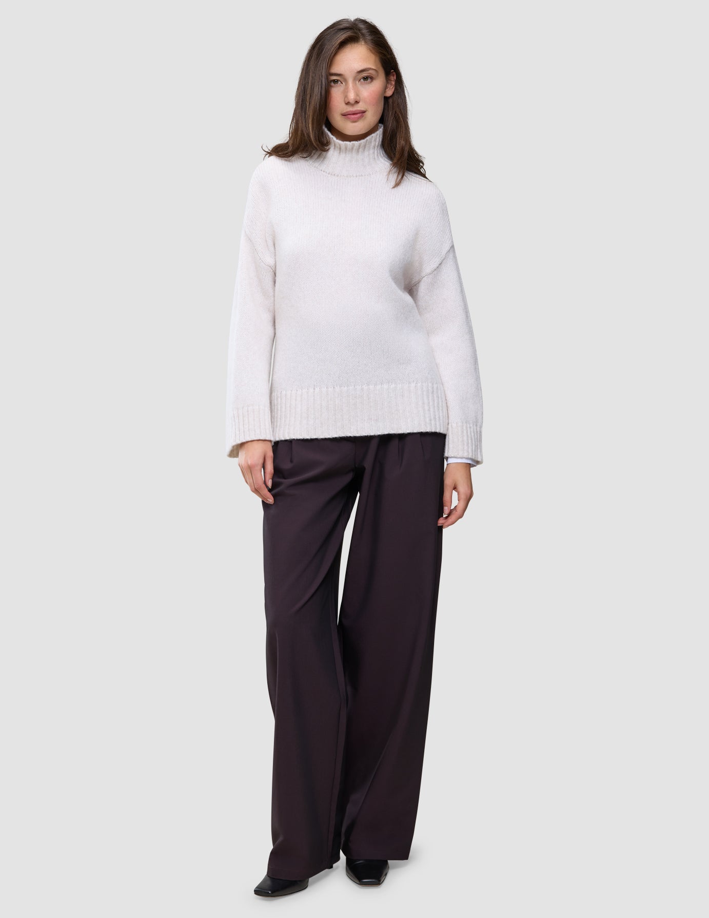 A woman wearing a Women’s Chunky Soft Wool Knit Turtleneck Sugar Melange in a cream-colored chunky wool, paired with dark wide-leg trousers.