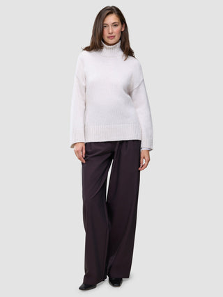 A woman wearing a Women’s Chunky Soft Wool Knit Turtleneck Sugar Melange in a cream-colored chunky wool, paired with dark wide-leg trousers.