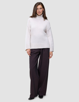 A woman wearing a Women’s Chunky Soft Wool Knit Turtleneck Sugar Melange in a cream-colored chunky wool, paired with dark wide-leg trousers.