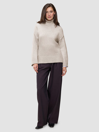 A person wearing a Women’s Chunky Soft Wool Knit Turtleneck Sugar Melange in beige and dark wide-leg trousers.