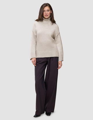 A person wearing a Women’s Chunky Soft Wool Knit Turtleneck Sugar Melange in beige and dark wide-leg trousers.