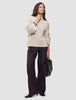 A woman wearing a Women’s Chunky Soft Wool Knit Turtleneck Sugar Melange in beige with wide-leg dark trousers, carrying a black handbag.