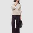 A woman wearing a Women’s Chunky Soft Wool Knit Turtleneck Sugar Melange in beige with wide-leg dark trousers, carrying a black handbag.