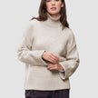 A woman wearing a Women’s Chunky Soft Wool Knit Turtleneck Sugar Melange, an oversized, light beige merino wool sweater with ribbed cuffs and hem, showcasing a minimalist Scandinavian design.