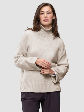 A woman wearing a Women’s Chunky Soft Wool Knit Turtleneck Sugar Melange, an oversized, light beige merino wool sweater with ribbed cuffs and hem, showcasing a minimalist Scandinavian design.