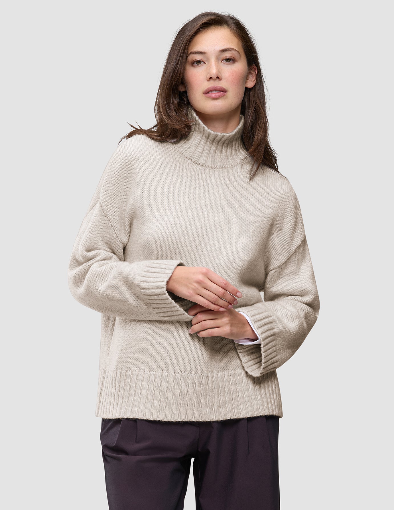 A woman wearing a Women’s Chunky Soft Wool Knit Turtleneck Sugar Melange, an oversized, light beige merino wool sweater with ribbed cuffs and hem, showcasing a minimalist Scandinavian design.