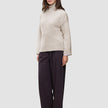 A woman wears a Women’s Chunky Soft Wool Knit Turtleneck Sugar Melange in beige with wide-leg dark trousers.