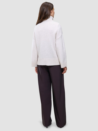 A person seen from behind, wearing an oversized, light-colored Women’s Chunky Soft Wool Knit Turtleneck Sugar Melange and wide-leg dark trousers.