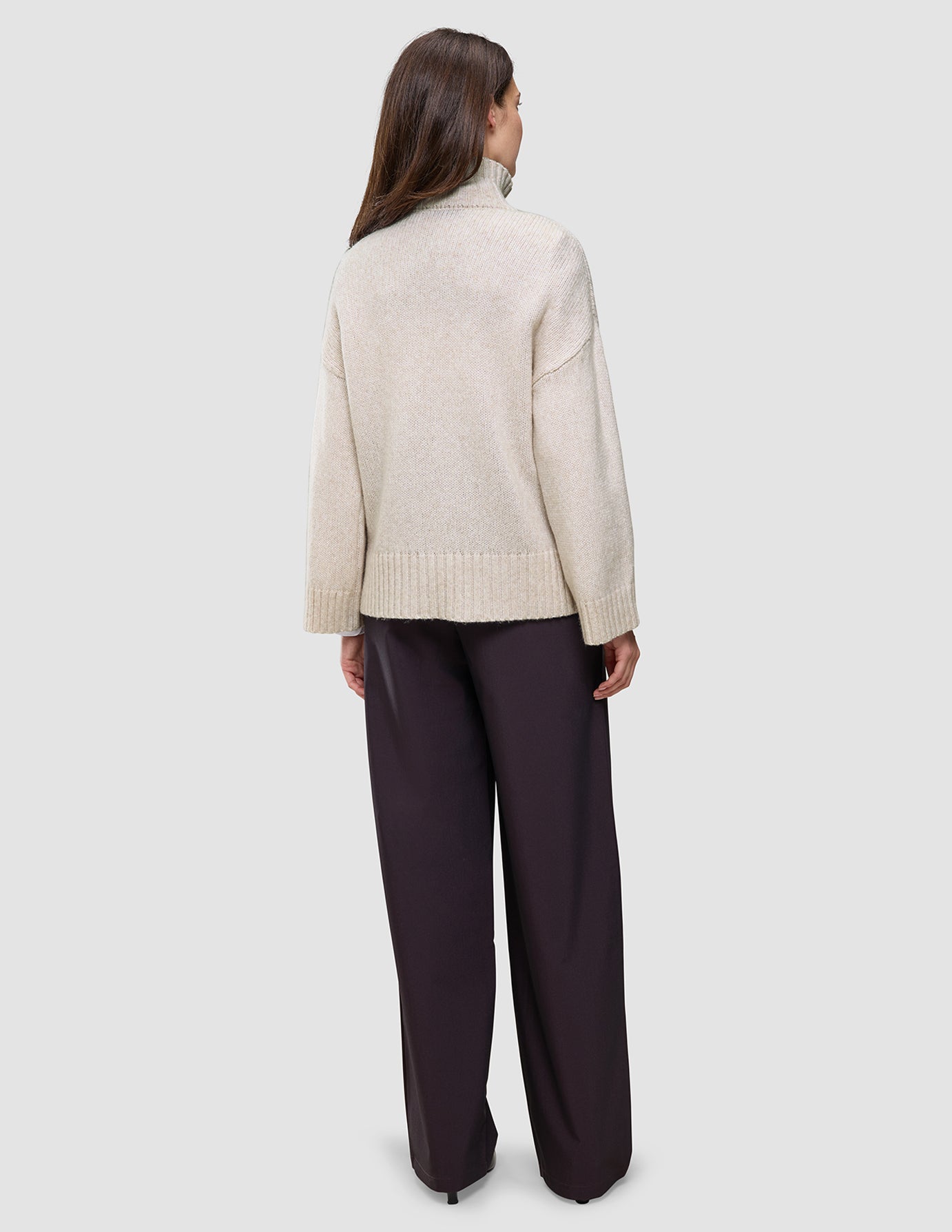 Back view of a person wearing a Women’s Chunky Soft Wool Knit Turtleneck Sugar Melange in an oversized, chunky knit style with dark wide-leg trousers.