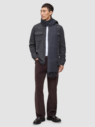 A man wearing a Double Layer Wool Overshirt Regular Dark Grey over a white shirt, a matching grey scarf, brown trousers, and dark loafers.