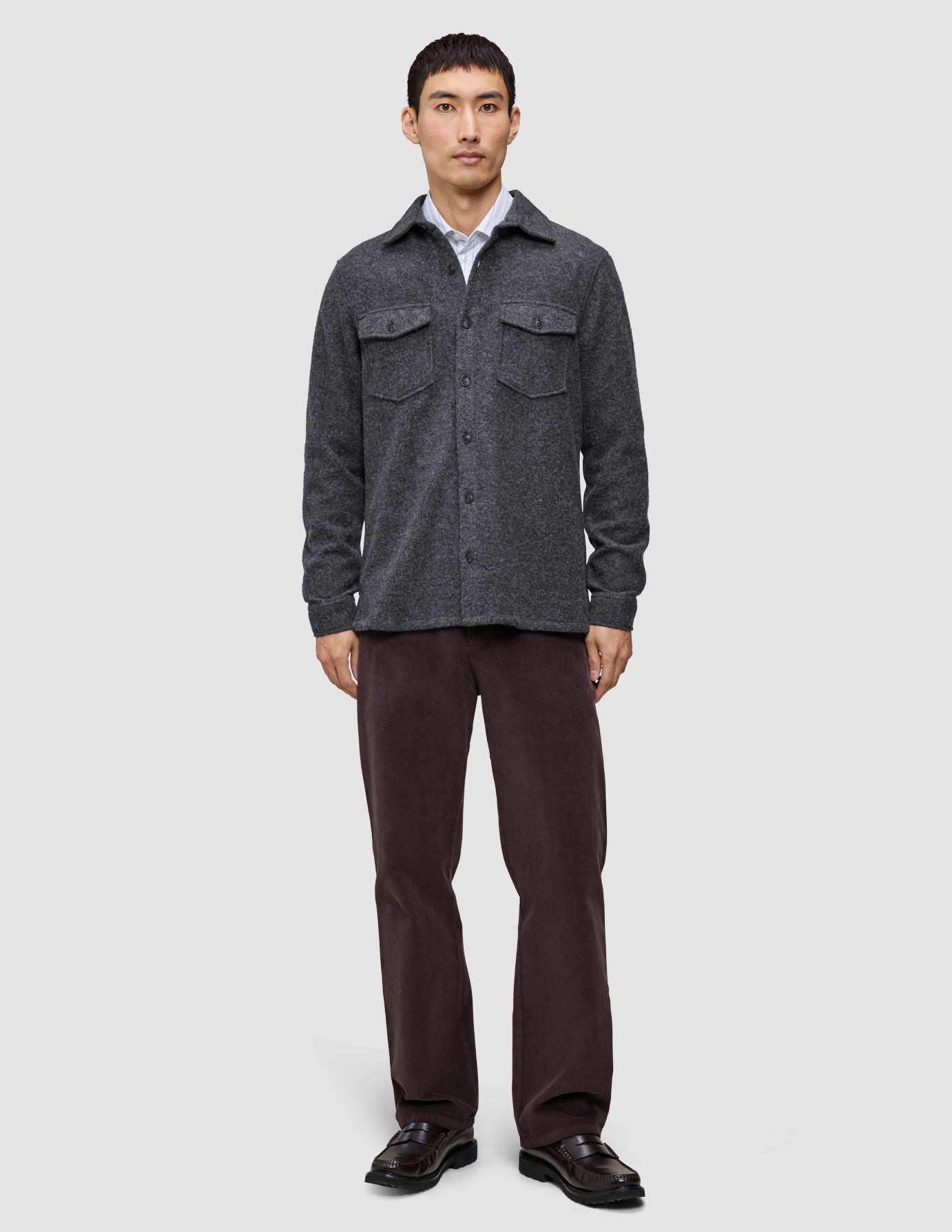 A man wearing a buttoned Double Layer Wool Overshirt Regular Dark Grey over a white collared shirt, paired with dark trousers and black loafers in a clean Scandinavian design.