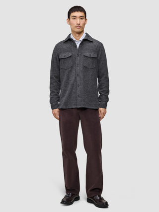 A man wearing a buttoned Double Layer Wool Overshirt Regular Dark Grey over a white collared shirt, paired with dark trousers and black loafers in a clean Scandinavian design.