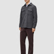 A man wears a Double Layer Wool Overshirt Regular Dark Grey over a white shirt, paired with dark brown trousers and dark loafers in a classic Scandinavian design.