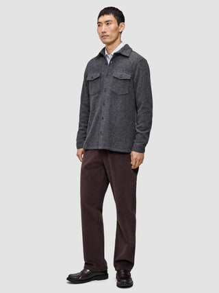 A man wears a Double Layer Wool Overshirt Regular Dark Grey over a white shirt, paired with dark brown trousers and dark loafers in a classic Scandinavian design.