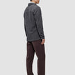 A man seen from the side wearing a Double Layer Wool Overshirt Regular Dark Grey, brown trousers, and dark loafers, showcasing a Scandinavian design aesthetic.