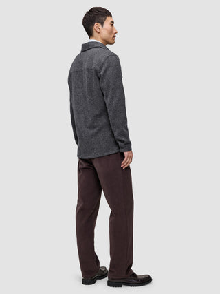 A man seen from the side wearing a Double Layer Wool Overshirt Regular Dark Grey, brown trousers, and dark loafers, showcasing a Scandinavian design aesthetic.