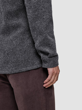 A person wearing a Double Layer Wool Overshirt Regular Dark Grey with long sleeves and brown trousers.