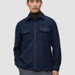 A man wears a Double Layer Wool Overshirt Regular Dark Navy over a brown turtleneck, showcasing a clean Scandinavian design with two chest pockets.