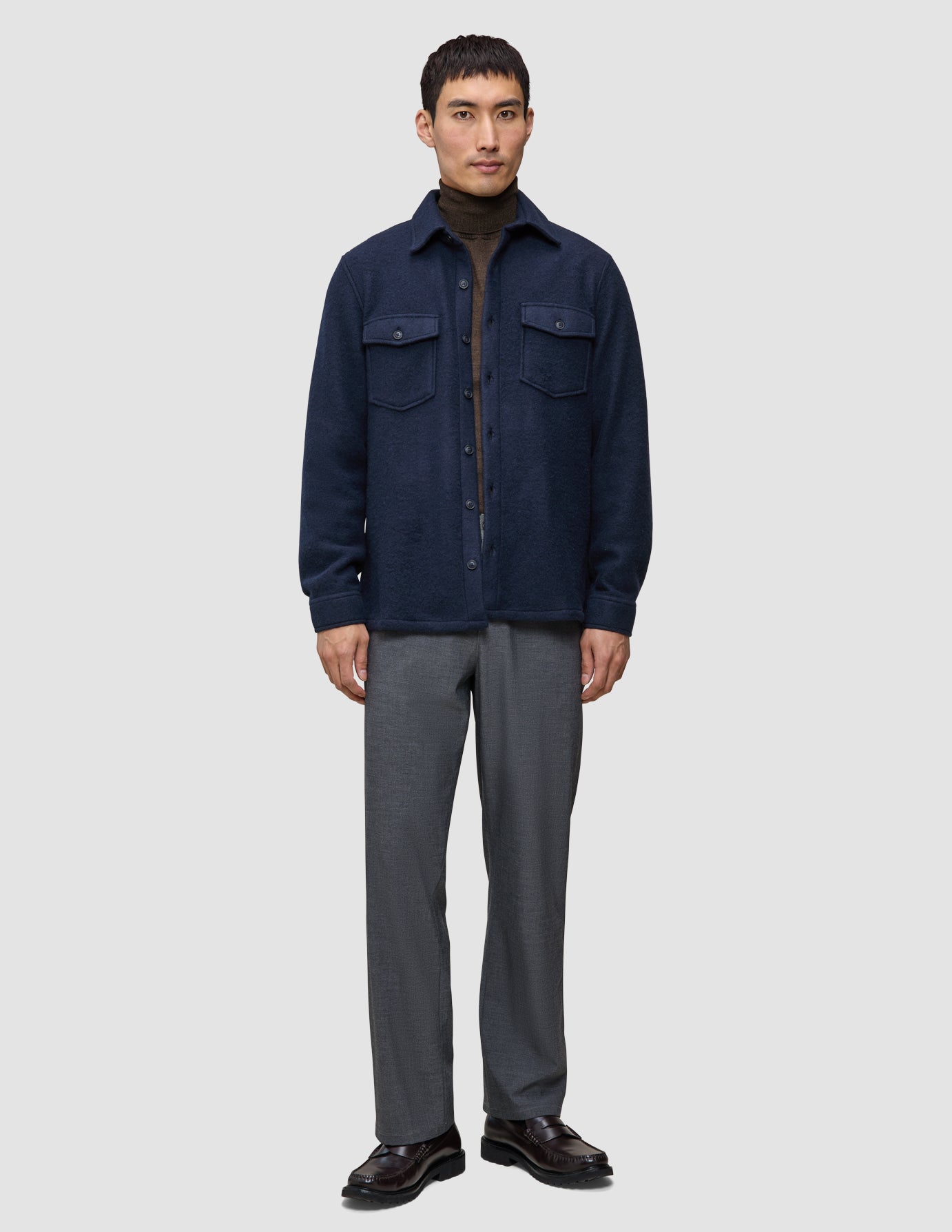 A man wearing a Double Layer Wool Overshirt Regular Dark Navy over a brown turtleneck sweater and grey trousers.